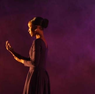 Dancer in purple with purple background looking at their hand.